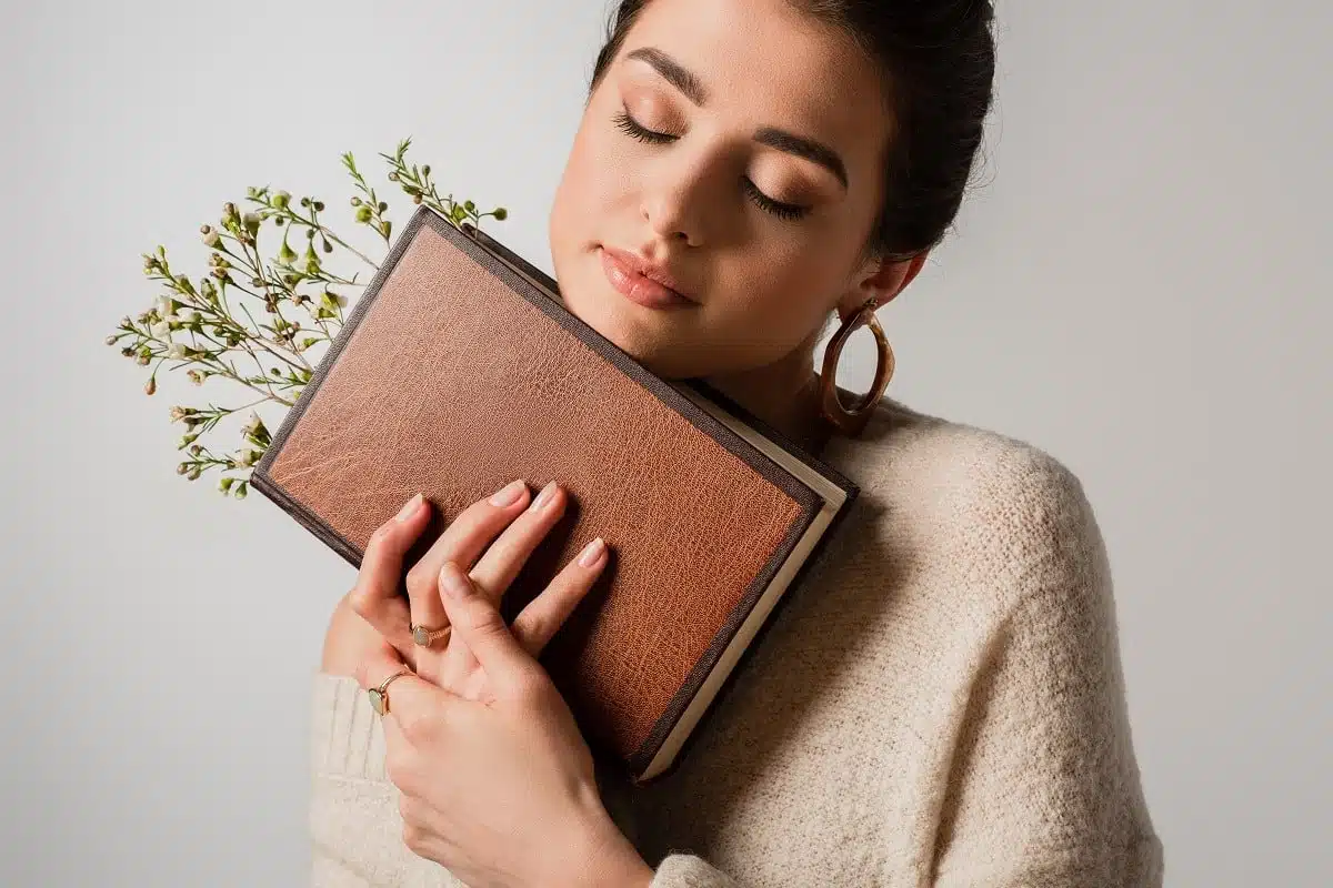Young woman with closed eyes holding book with inserted wildflowers.