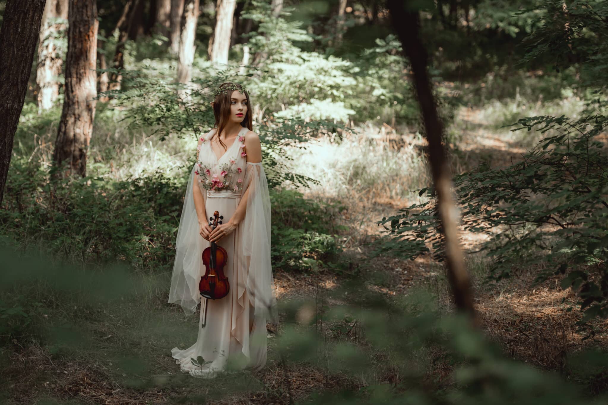 mystic elf in elegant dress holding violin in beautiful forest.
