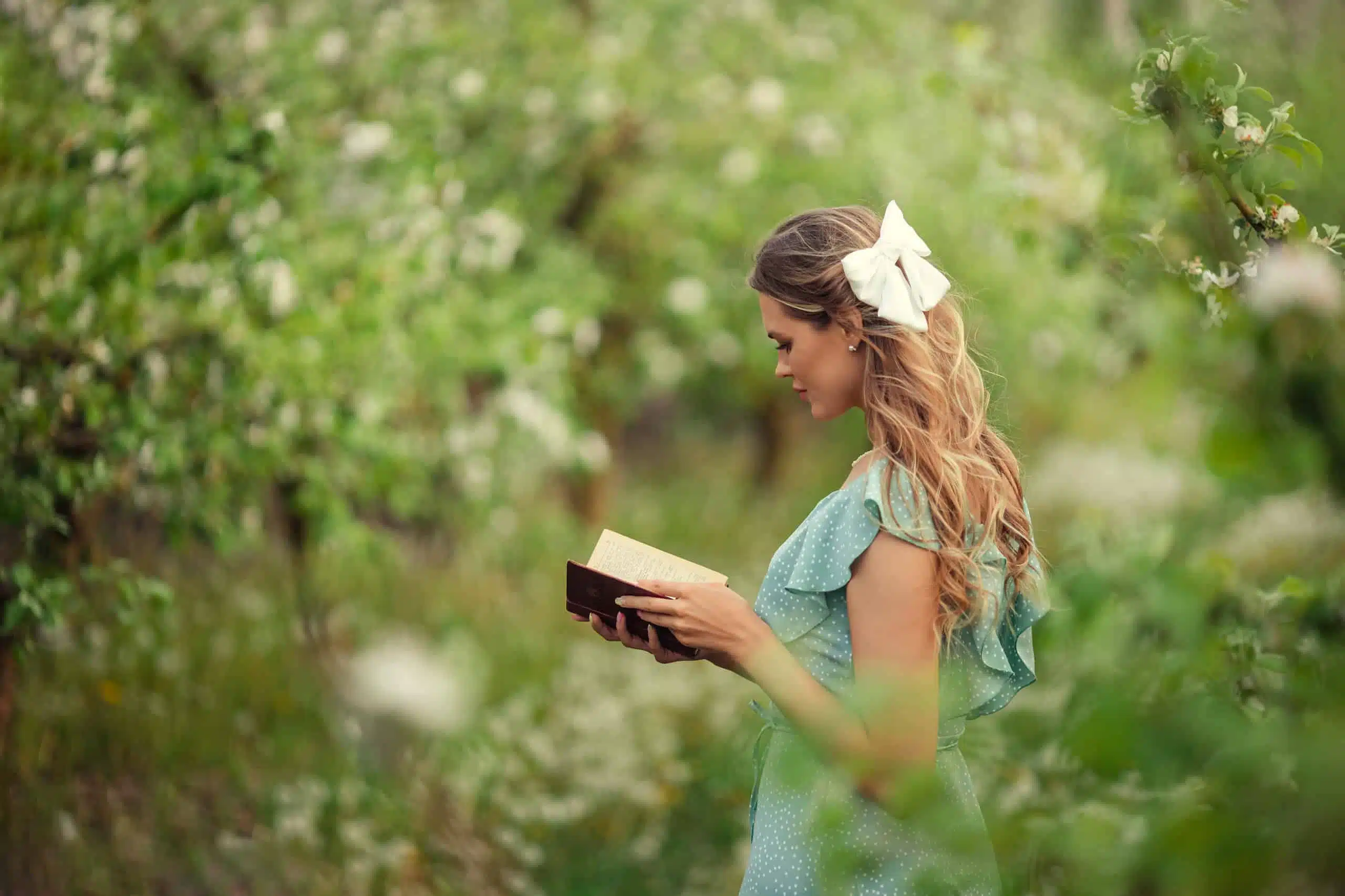 Beautiful young woman in a romantic dress reads a book outdoor.