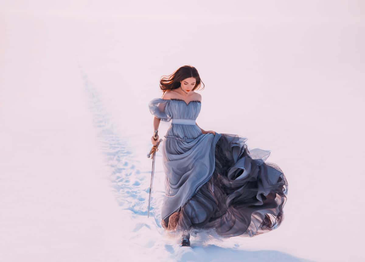 Fantasy lonely princess redhead hair elf walks winter frost white snow nature. Young beauty woman runs. queen holds hands magic blade sword. Blue silk long vintage dress fluttering fly wind in motion