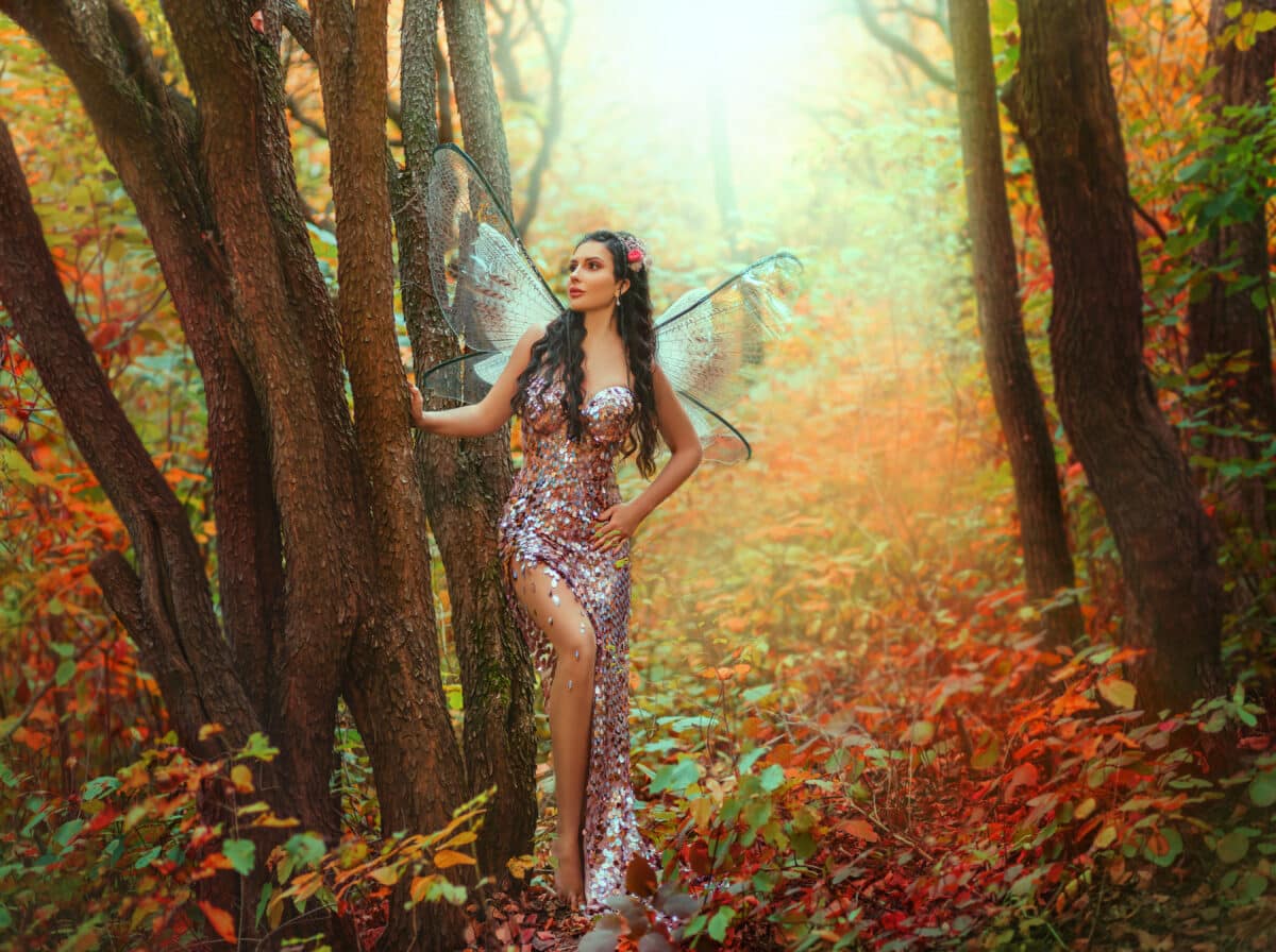 fantasy woman fairy, pixie wings creative costume. Girl angel forest goddess butterfly sexy elf. Magic light autumn nature wood orange foliage trees magic fog glow. Pink sparkle shining evening dress