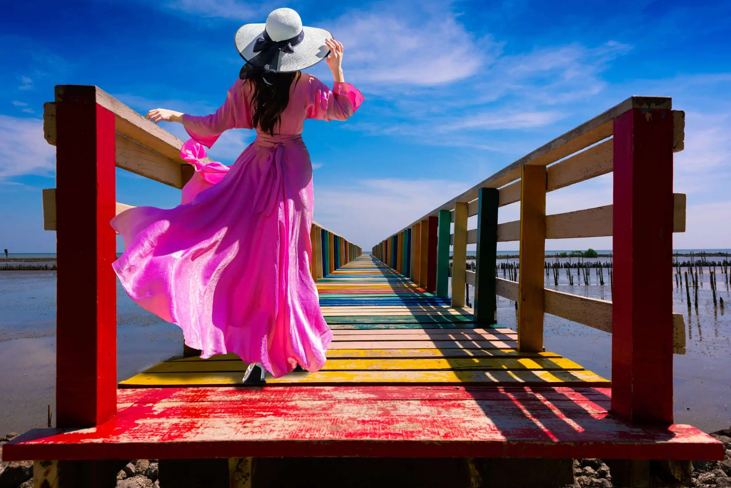 woman wearing purple dress standing on a colorful wooden bridge over the lake