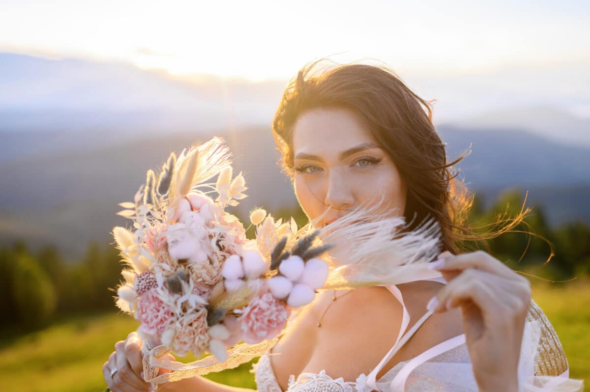Woman in wedding dress with buch of flowers on sunny landscapes background