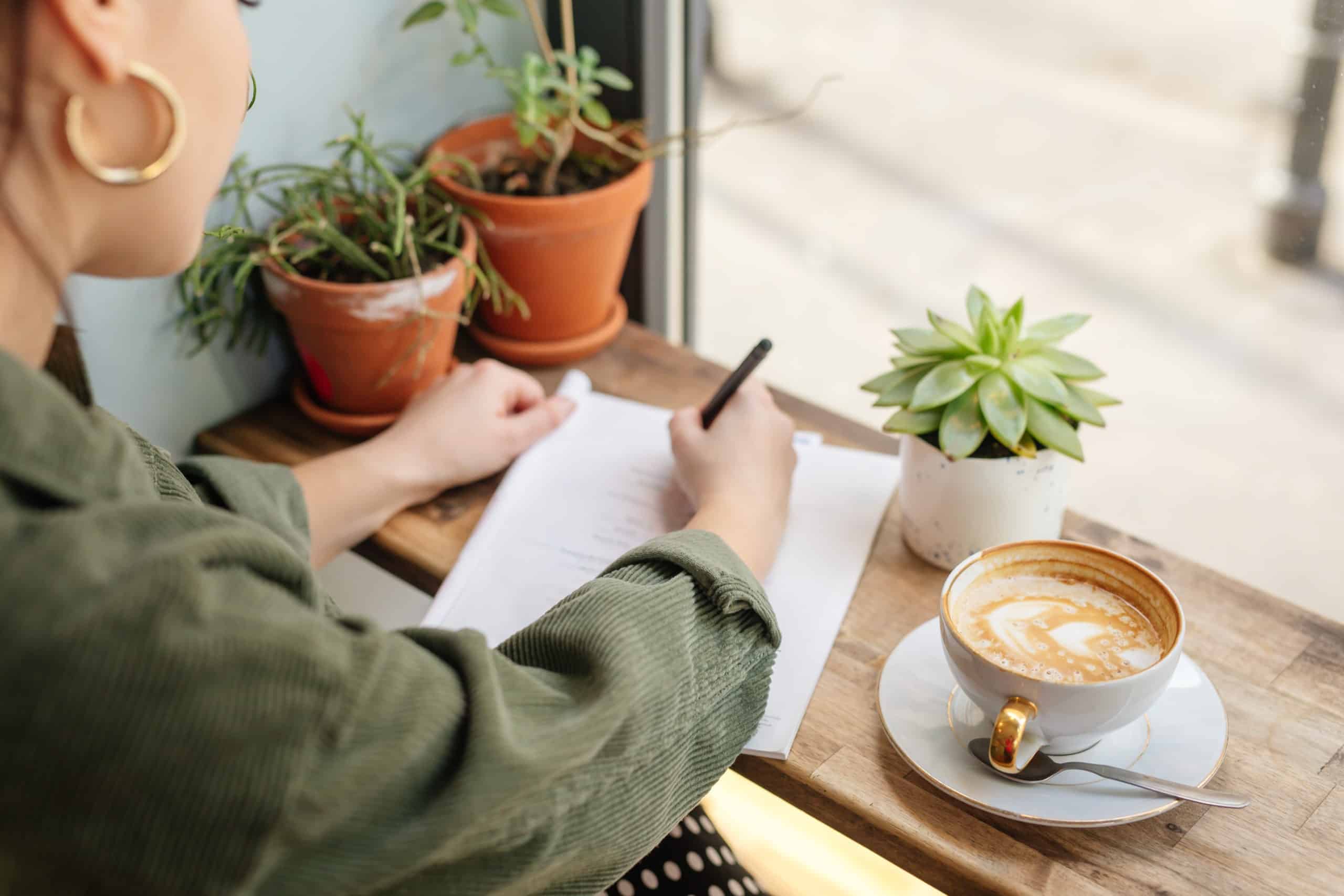 Woman sits at office writing, having coffee