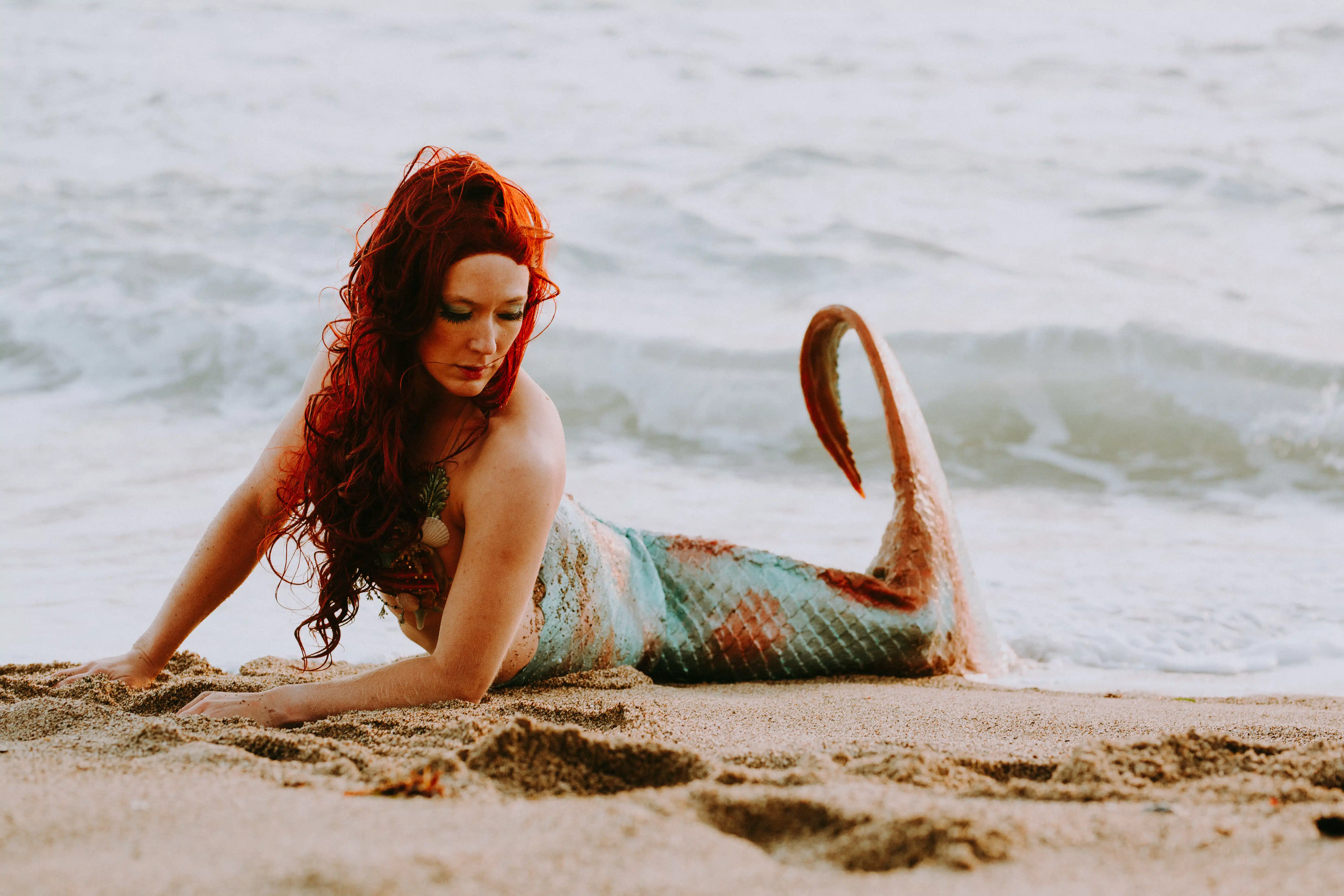 a red-haired mermaid resting on the beach