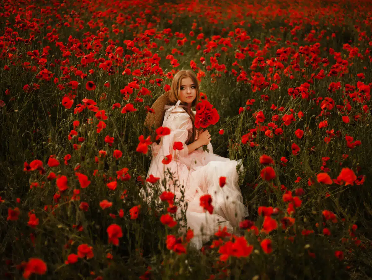 Young beautiful girl posing on poppy field in straw hat