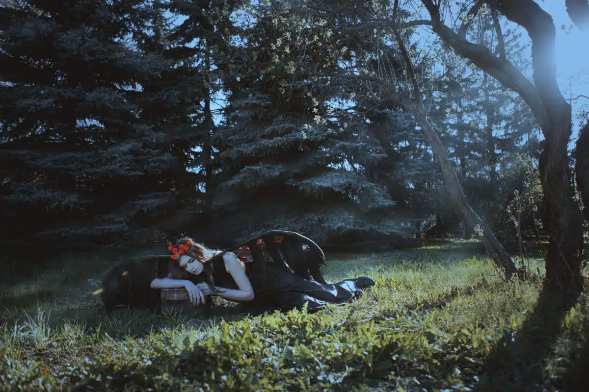 Young dark haired woman in dark clothes and wings lying in the misty woods