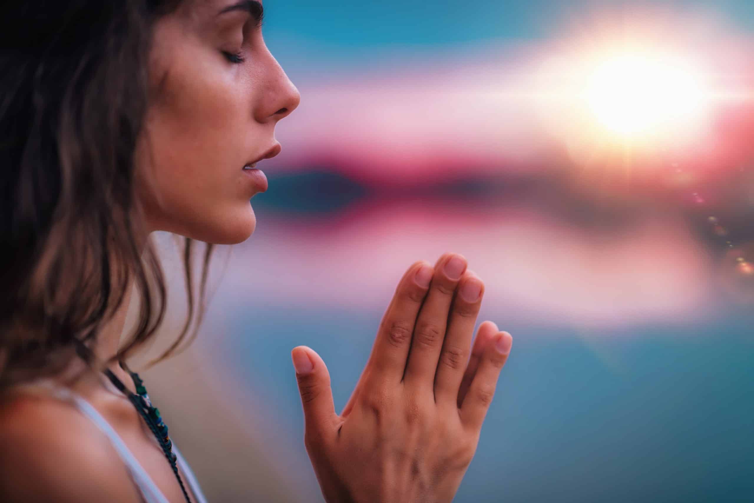 Woman eyes closed, hands clasped together in prayer position outdoors.