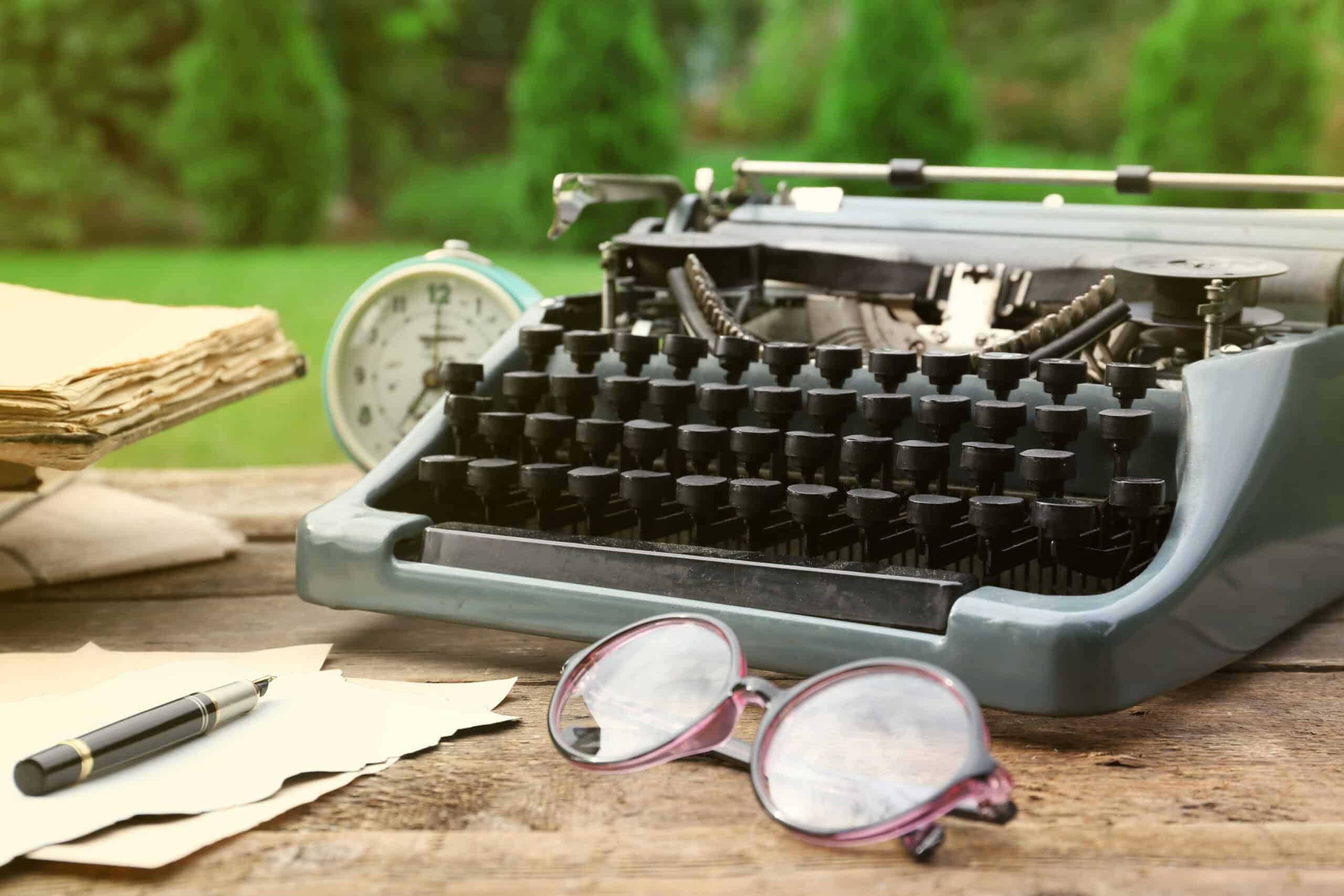 Vintage black typewriter with papers and pen on wooden table, outdoor