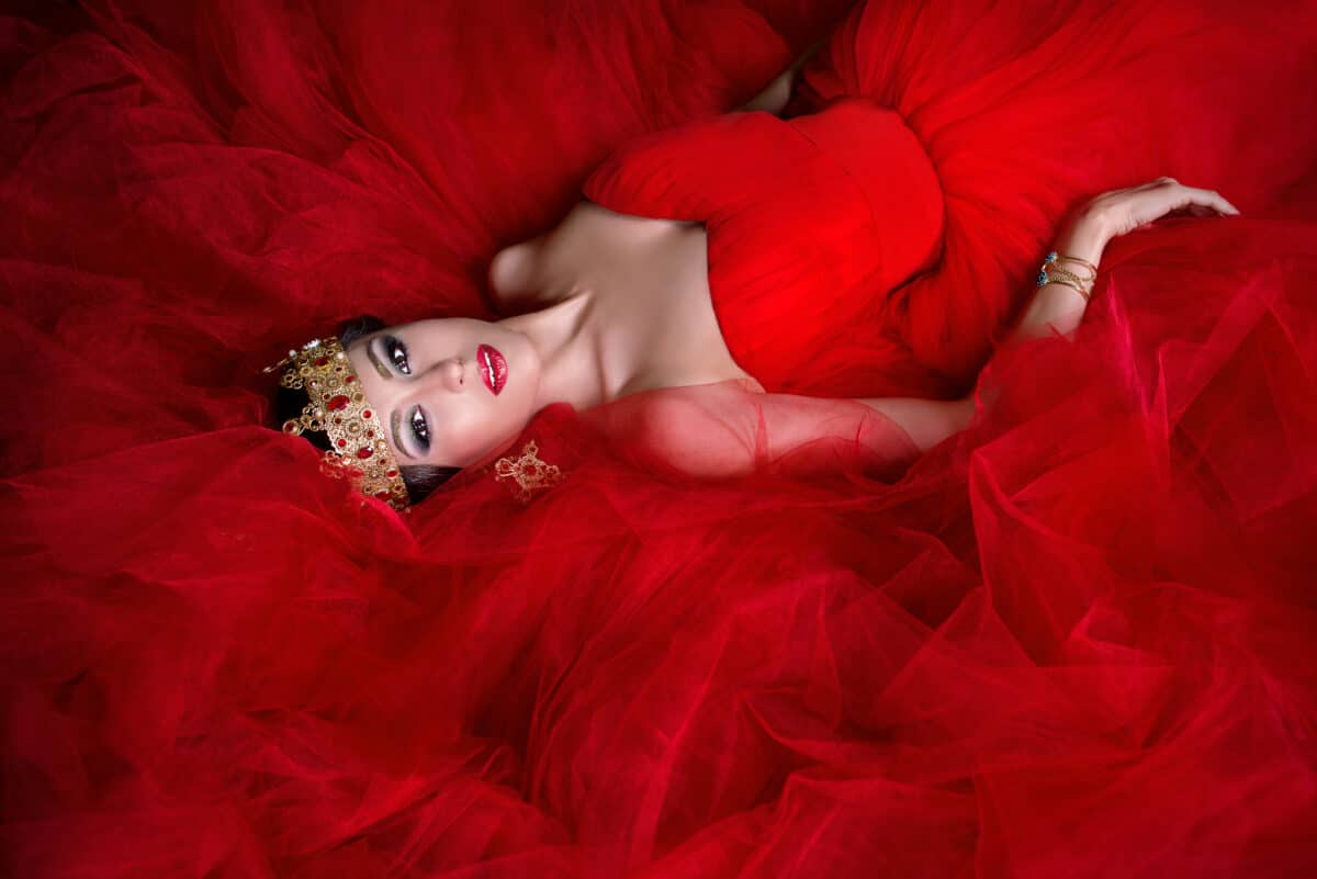 Beautiful girl in long red dress and in royal crown lying on the ground