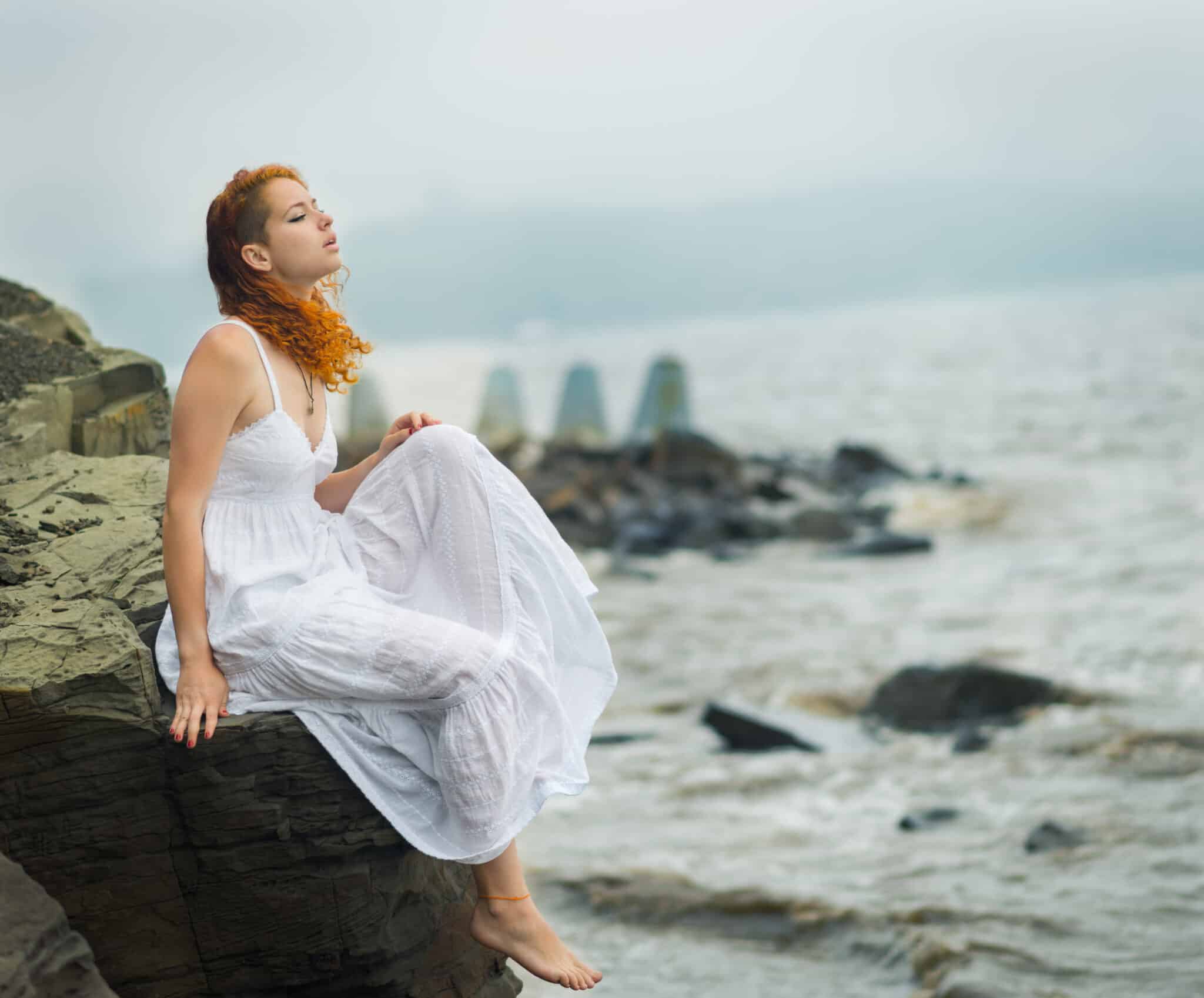 melancholic red-haired woman sitting on the coast on beach