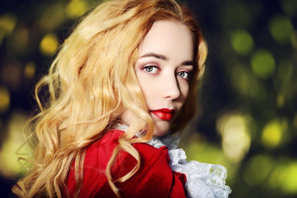a stunning blonde lady in a medieval dress and red cloak in a fairy forest