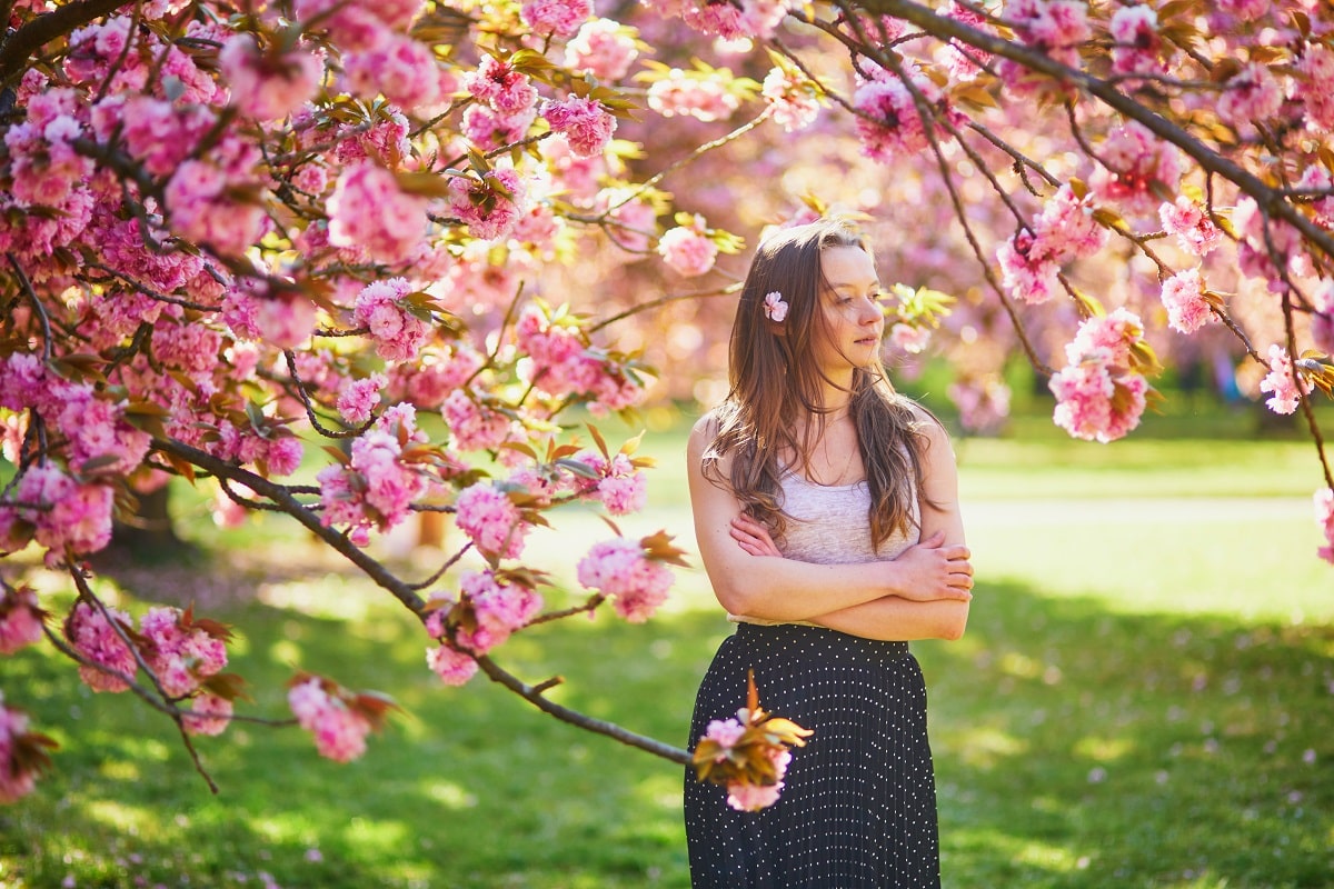 Beautiful young woman on sunny spring day in park during cherry blossom season.