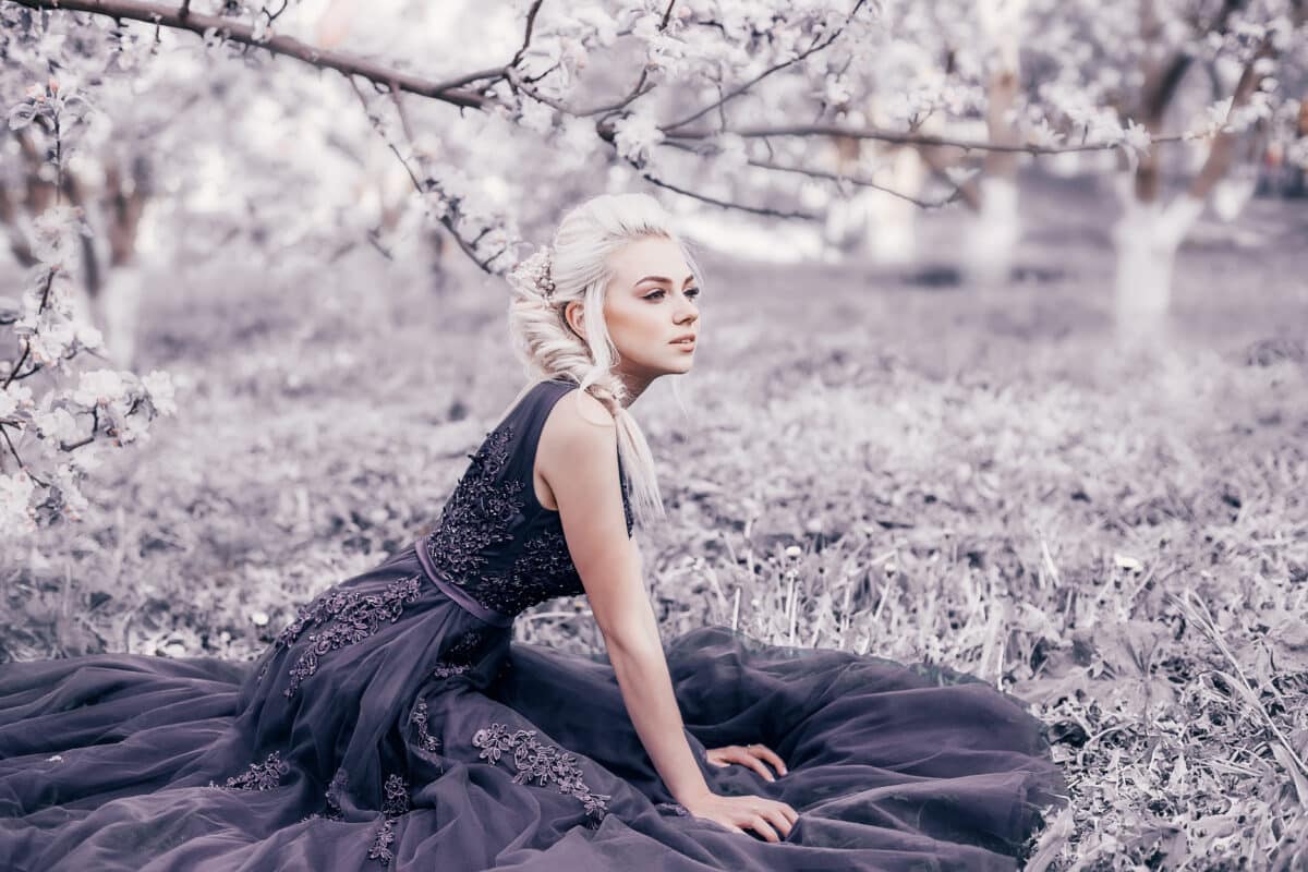 Beautiful woman in a long purple dress in a spring park with blooming trees. Violet toned.