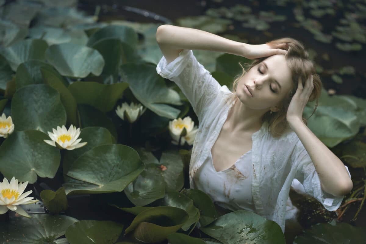 enchanting blond woman in a pond among white water lilies