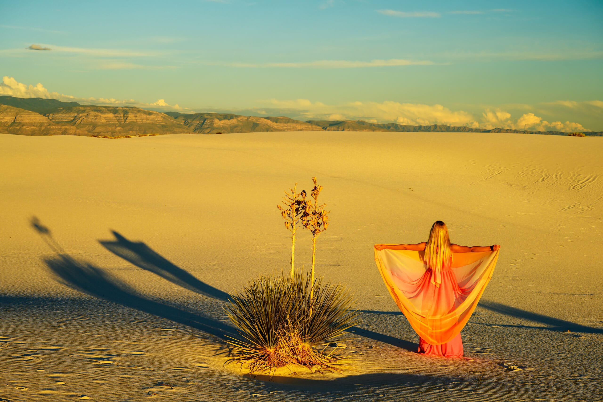 Elegant woman, wearing a fancy dress and standing like a fairy among the yuccas and dunes in the desert