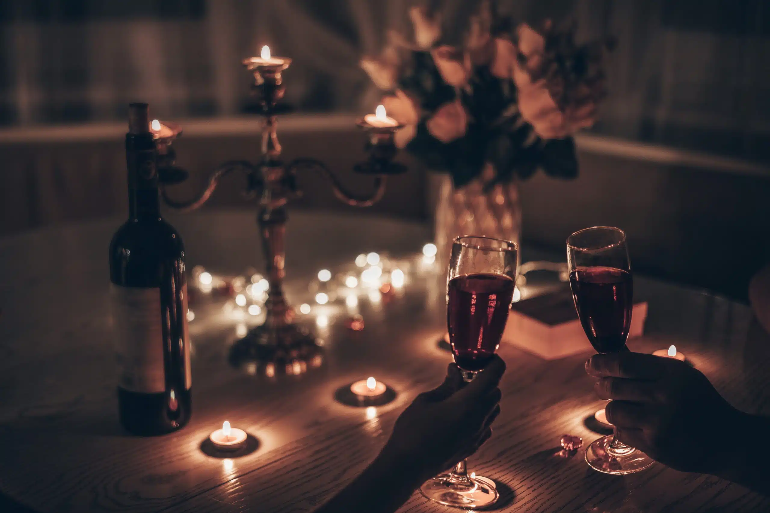 Hands man and woman holding glasses of wine having romantic candlelight dinner at table at home.