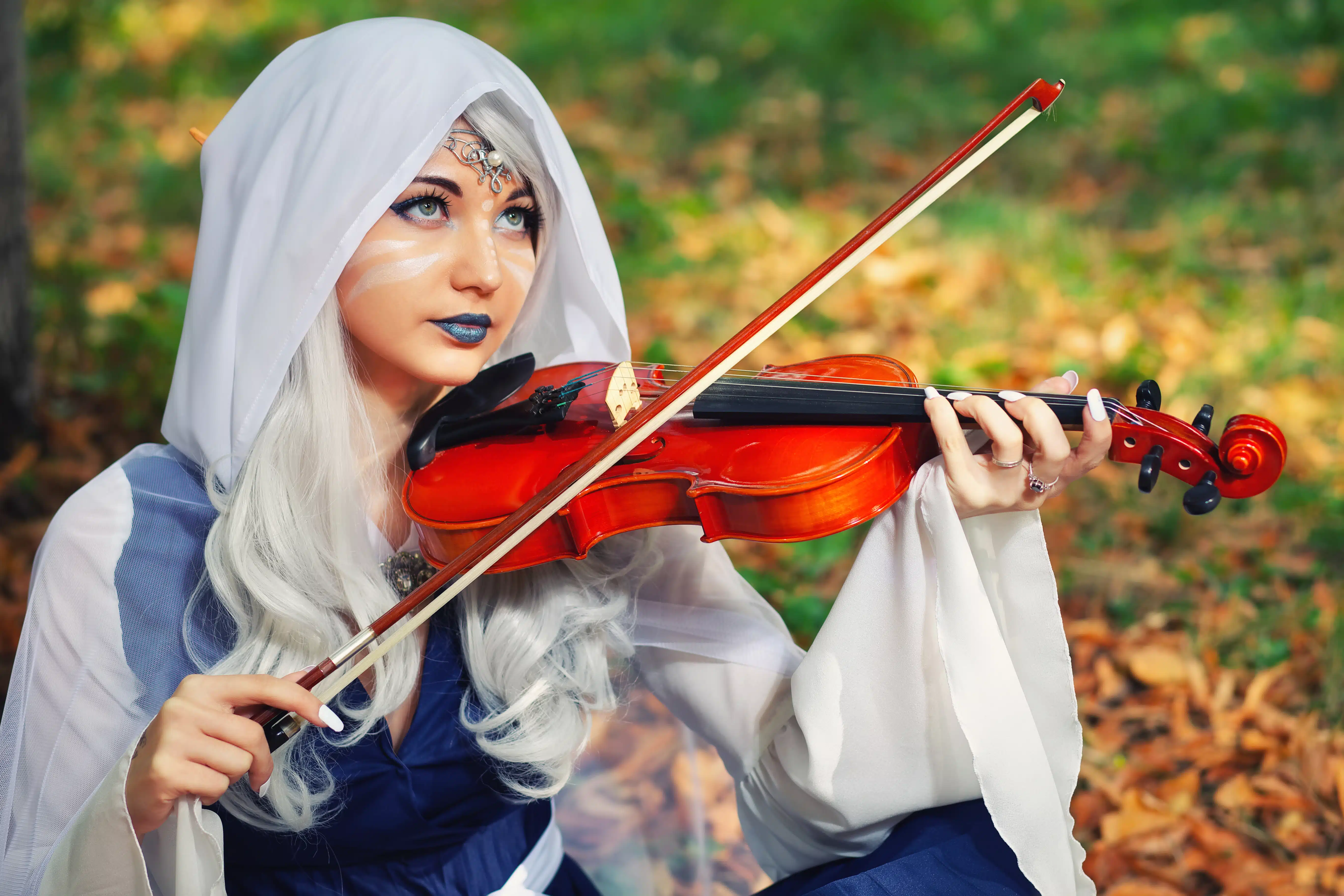 Elf with a violin in the autumn forest. Beautiful Girl In an elf costume playing a musical instrument.