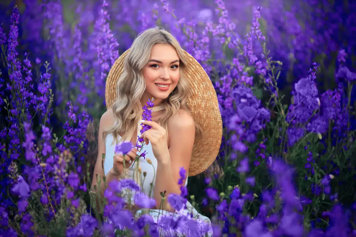 beautiful young girl in a white dress and a straw hat on a field of purple flowers