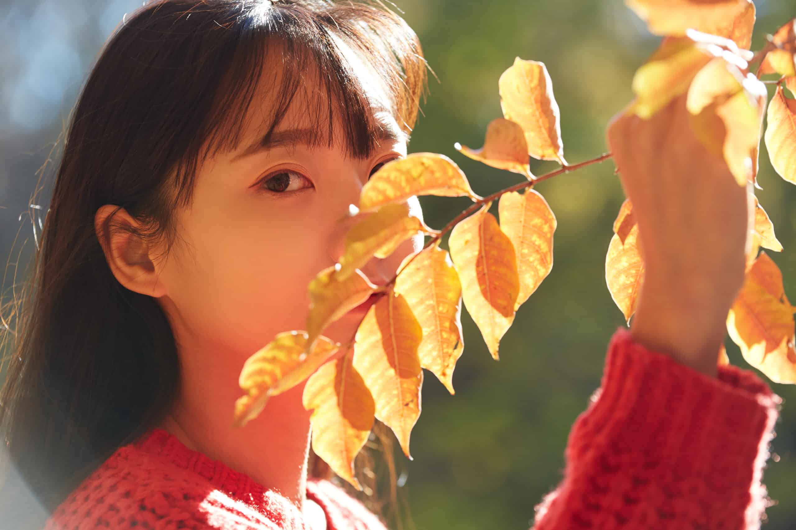 Japanese girl face hidden behind the leaves on a twig