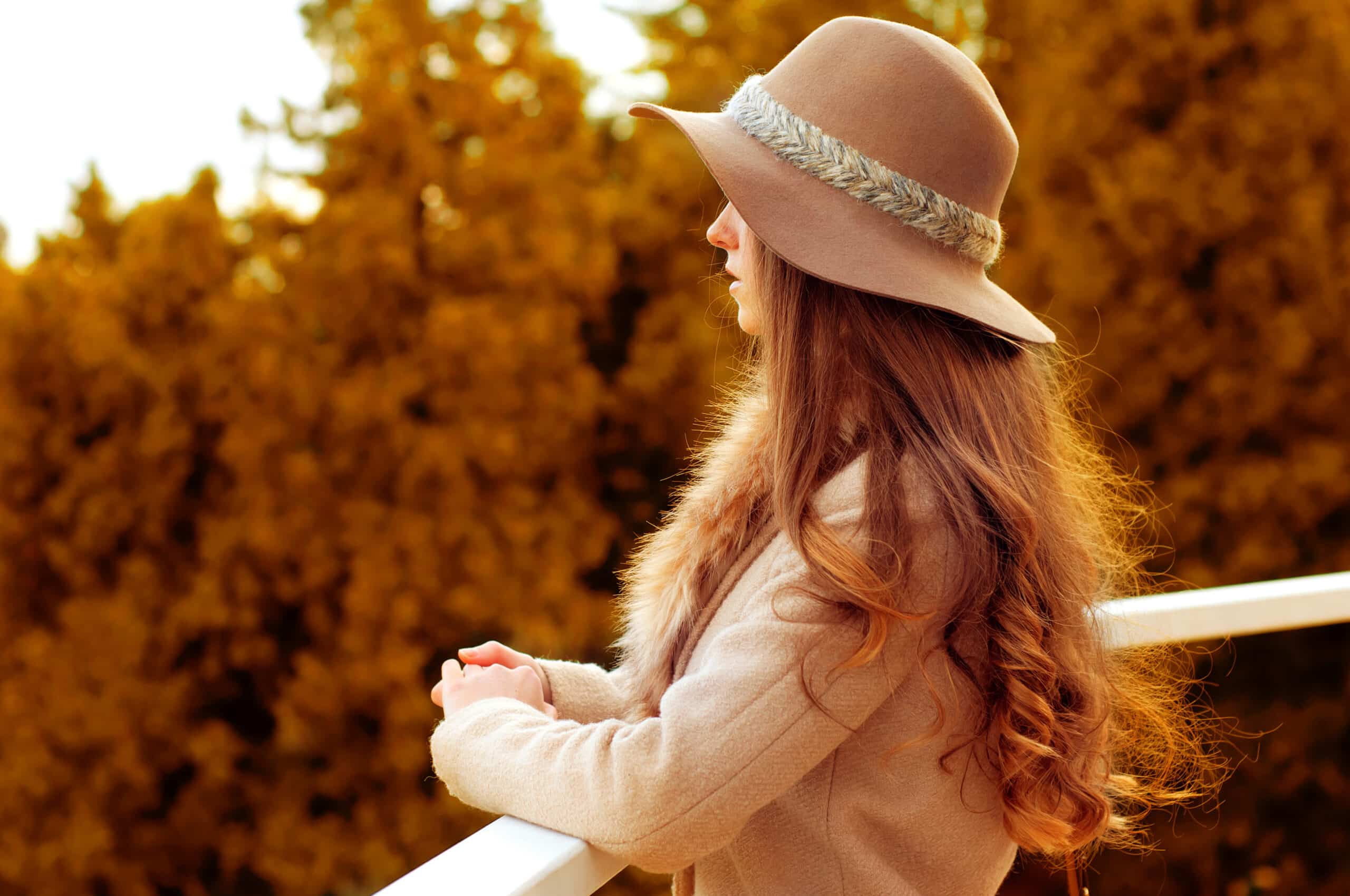 melancholic female redhead wearing a fedora hat and fur coat, standing on a bridge looking far ahead