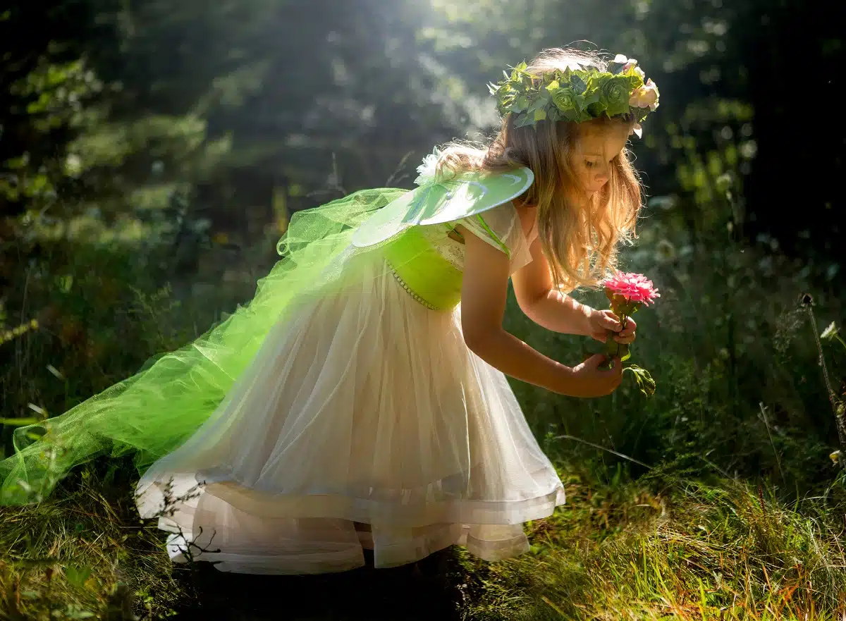 little fairy girl bowing down to the ground holding a red flower in the woods