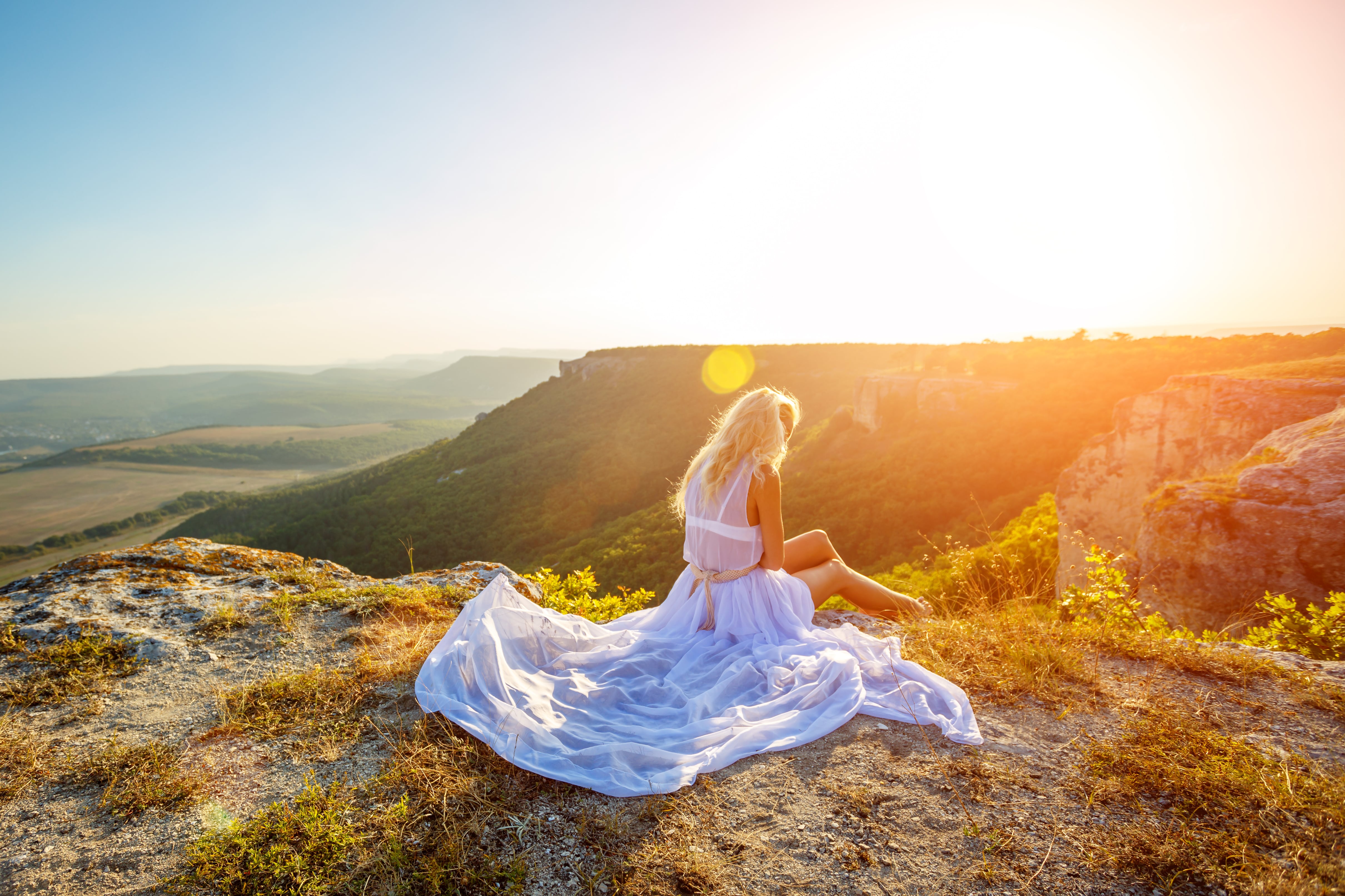a lonely woman sits on a rock on a mountain and looks at the beautiful view at sunset