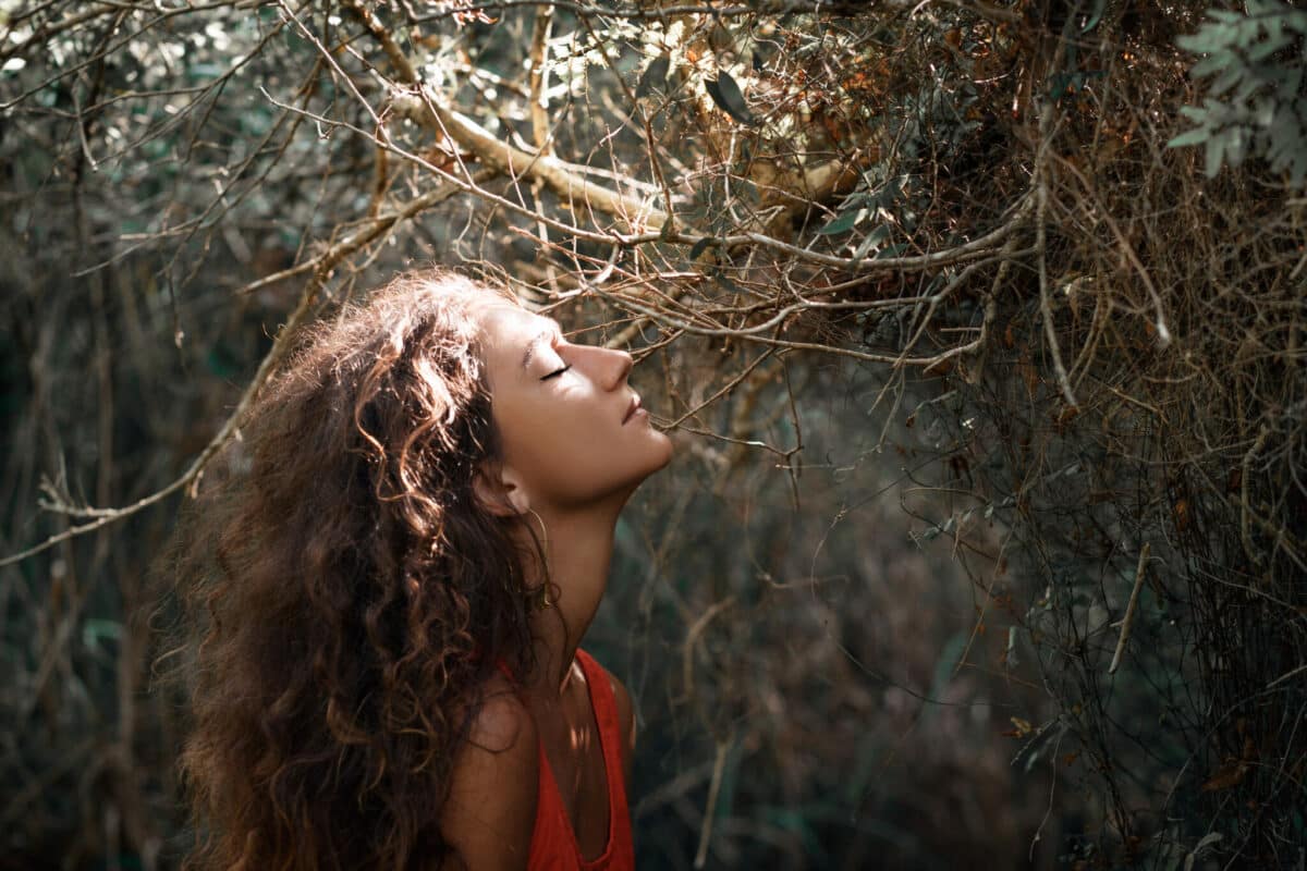 beautiful young woman in forest raising her head to the sunlight
