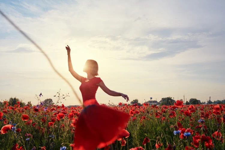  Pretty young woman in red dress dancing like ballerina in poppy field
