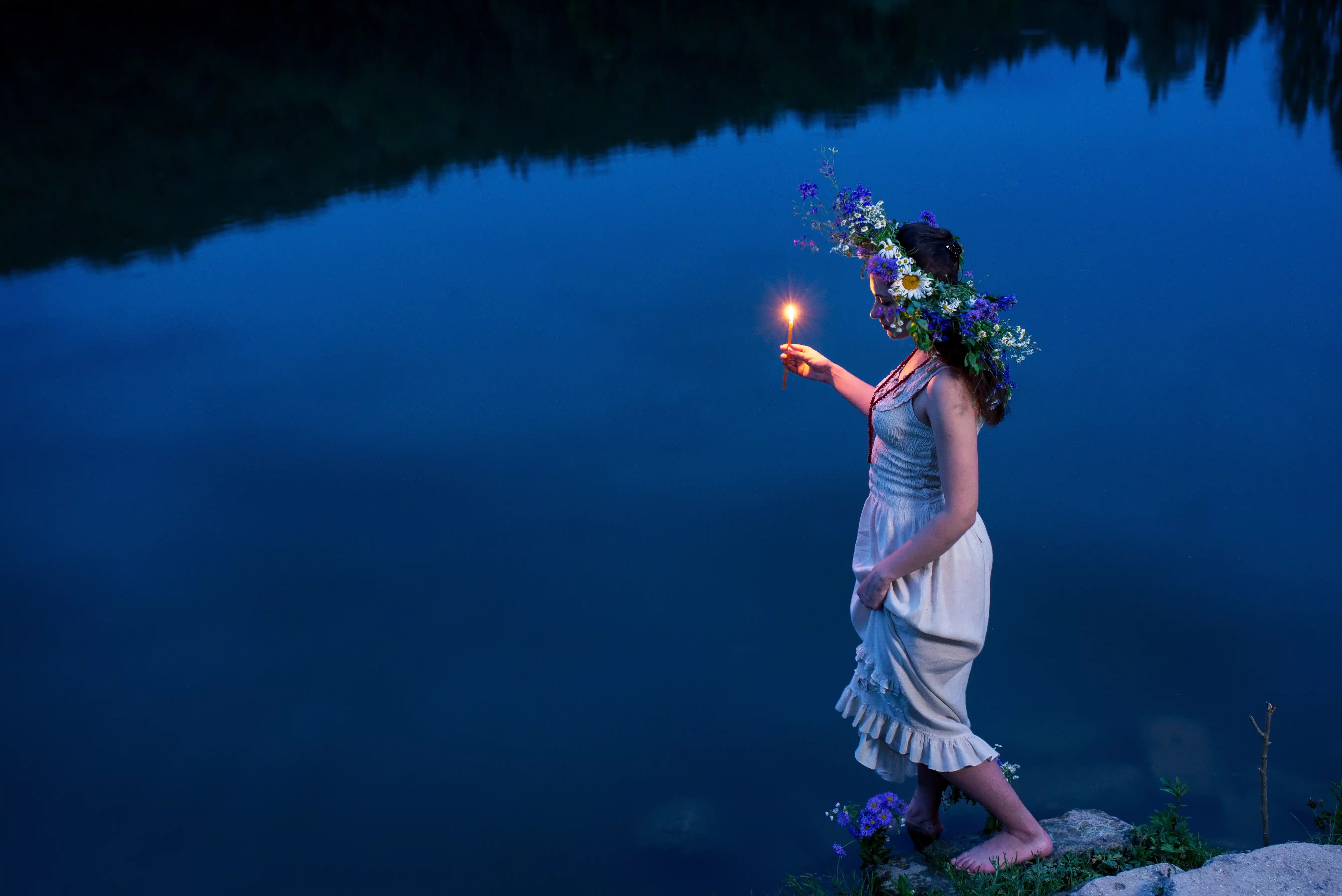 barefoot girl wearing a head wreath with a candle walks to the river