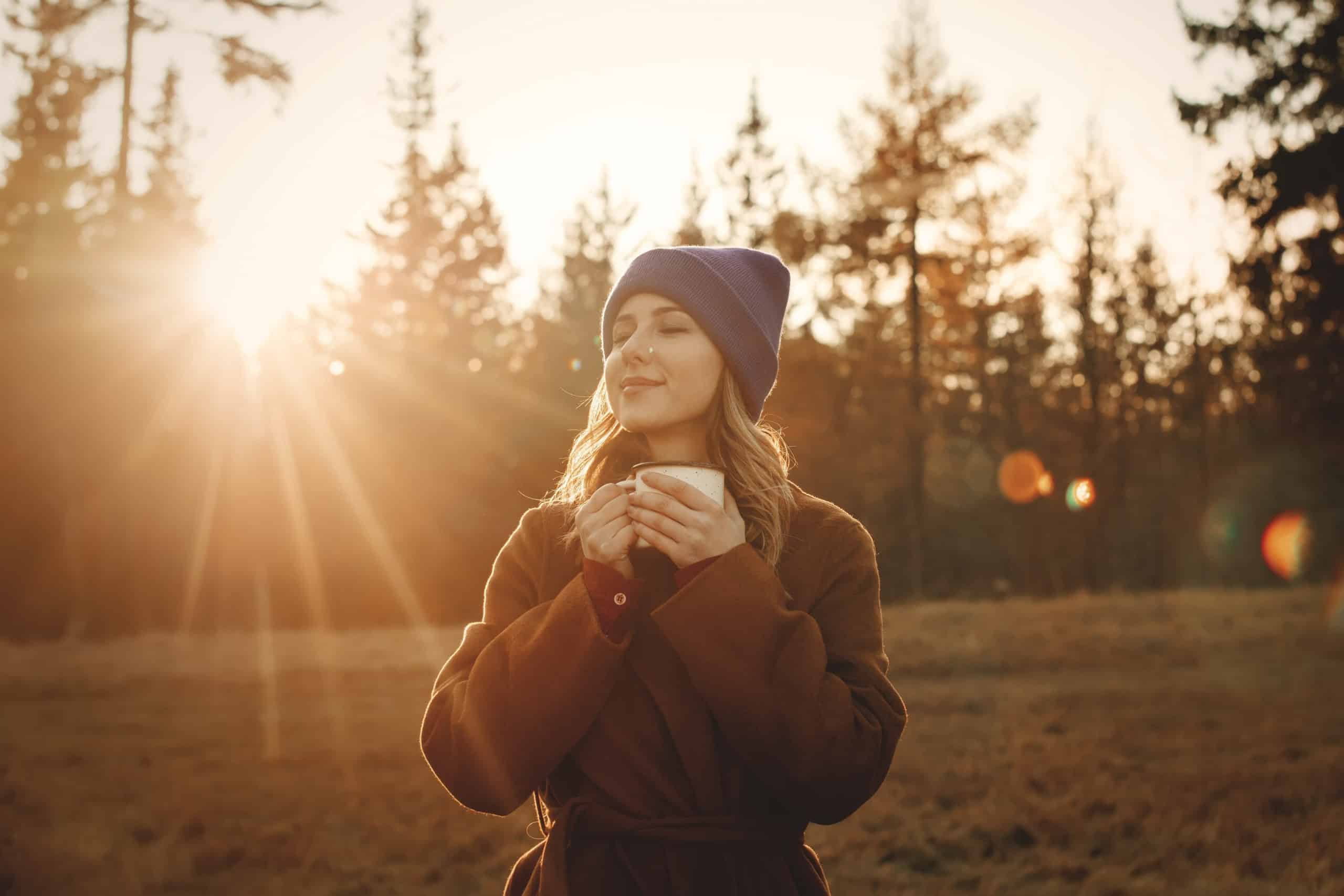 Young woman with cup of coffee stay near wood in sunset time.
