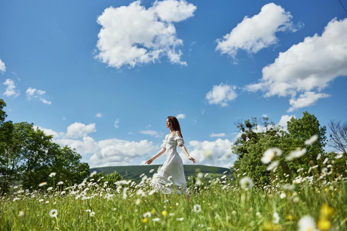 a woman in a light dress runs far across a chamomile field against a blue sky, enjoying harmony with nature
