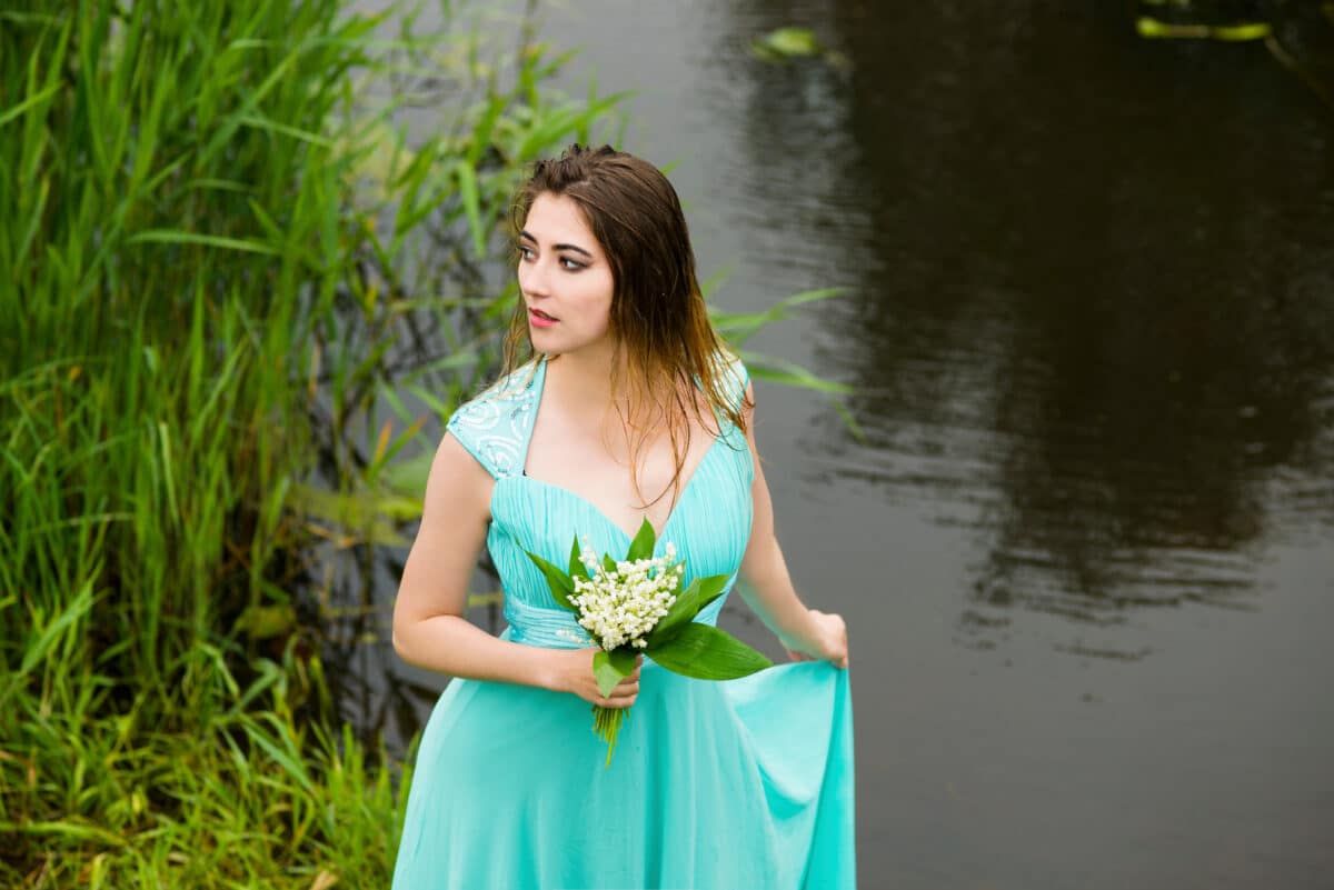 a woman with lilies of the valley standing on the river bank in summer