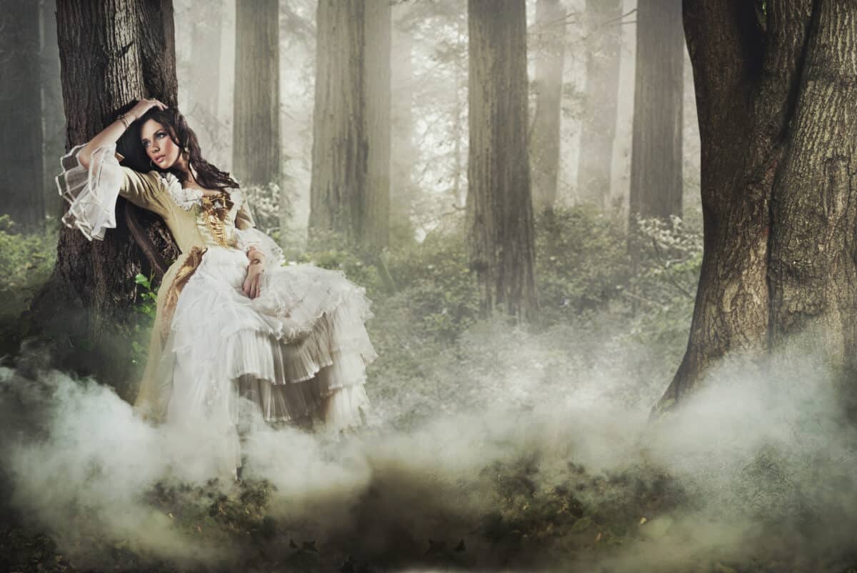 gorgeous lady in a white dress leaning against a tree in a mysterious foggy forest