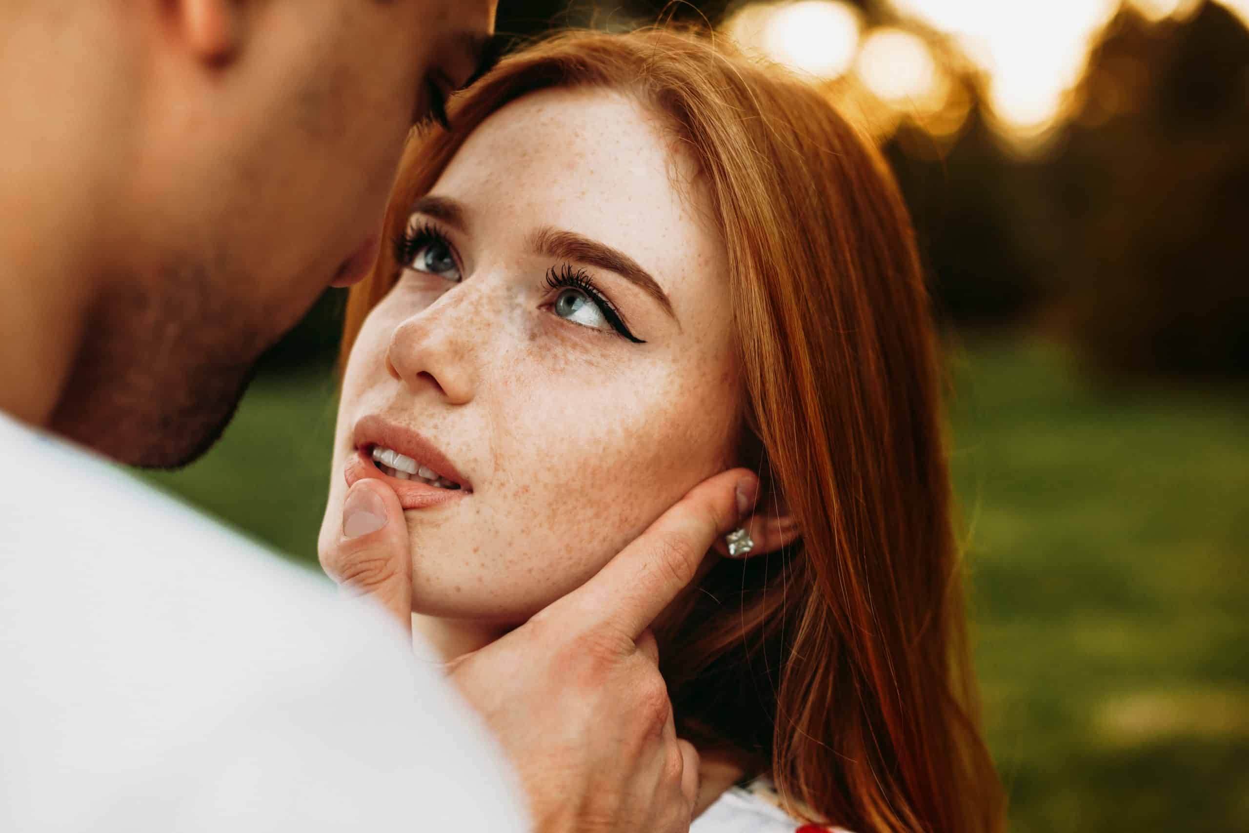 A red haired woman and green eyes looking at boyfriend touching her lips.