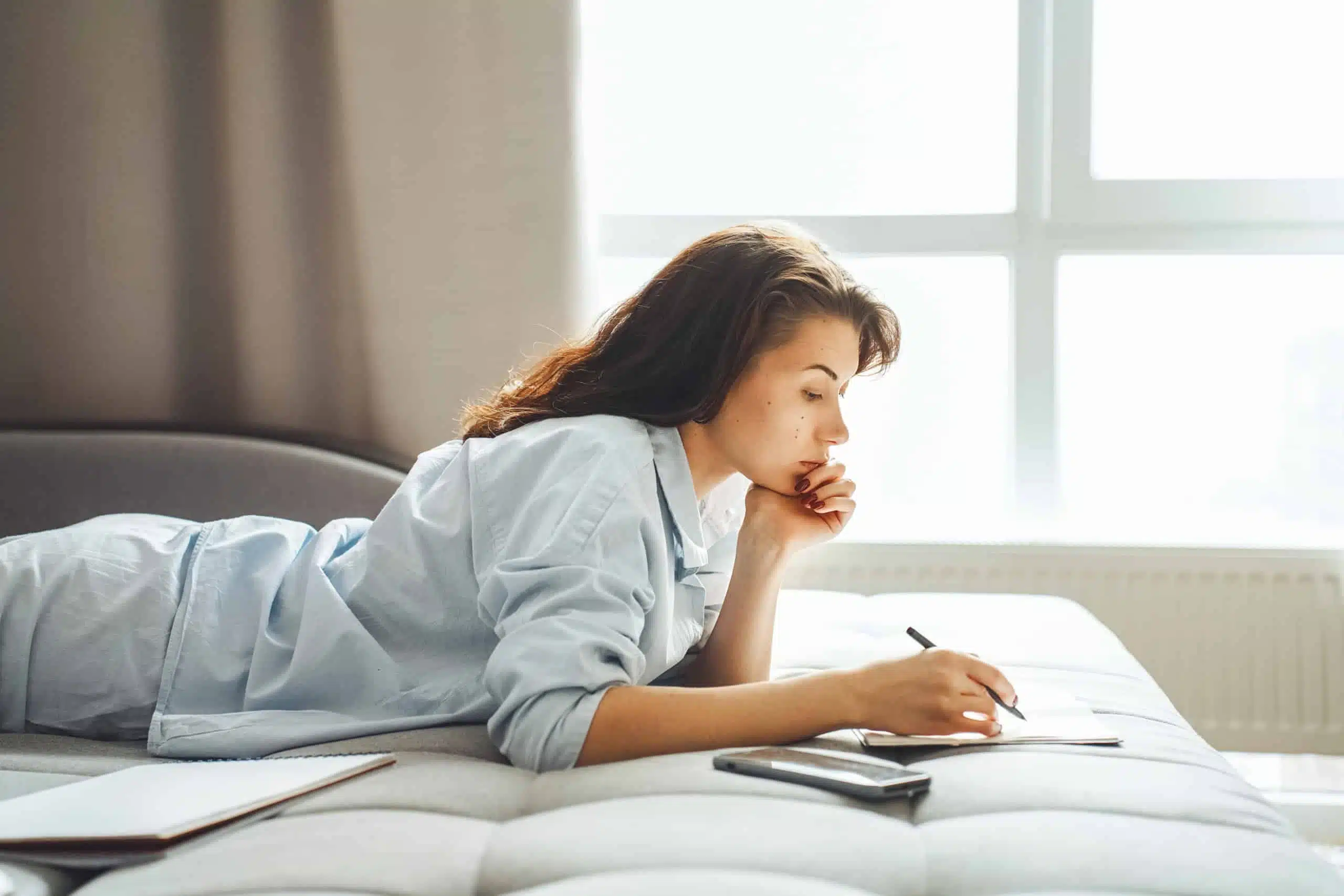 Woman lying on a bed at home working on a paper.