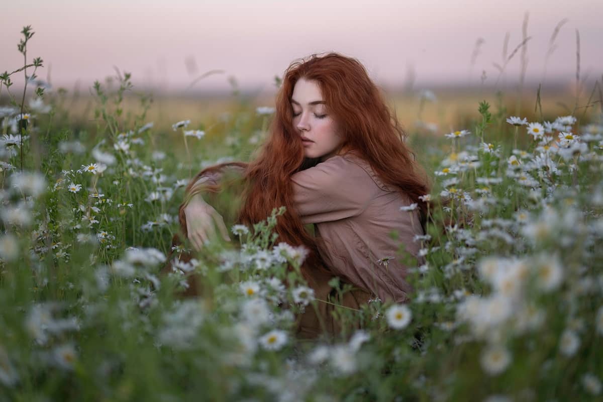 A red-haired girl is sitting among daisies