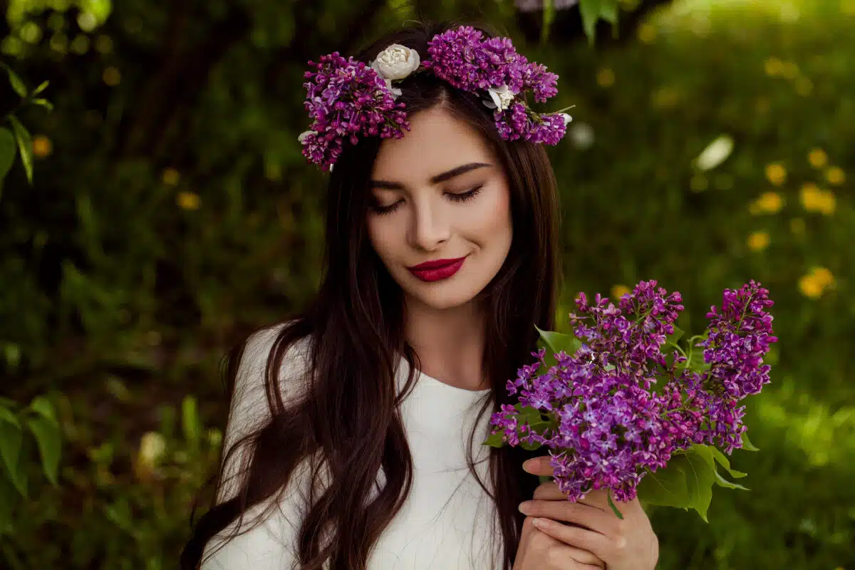 Smiling woman relaxing outdoors, summer portrait. Beautiful female model with makeup, long brown hair and lilac flowers