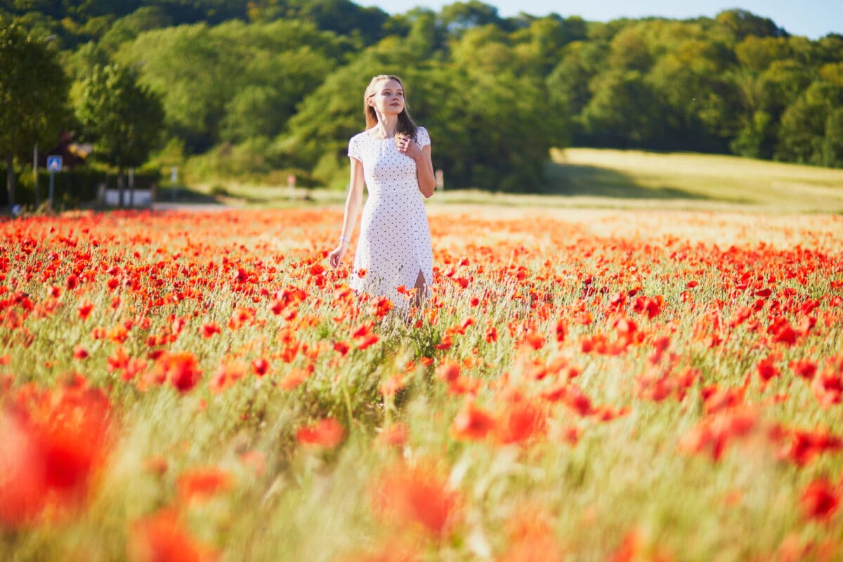 a beautiful young woman in white dress walking in poppy field on a summer day