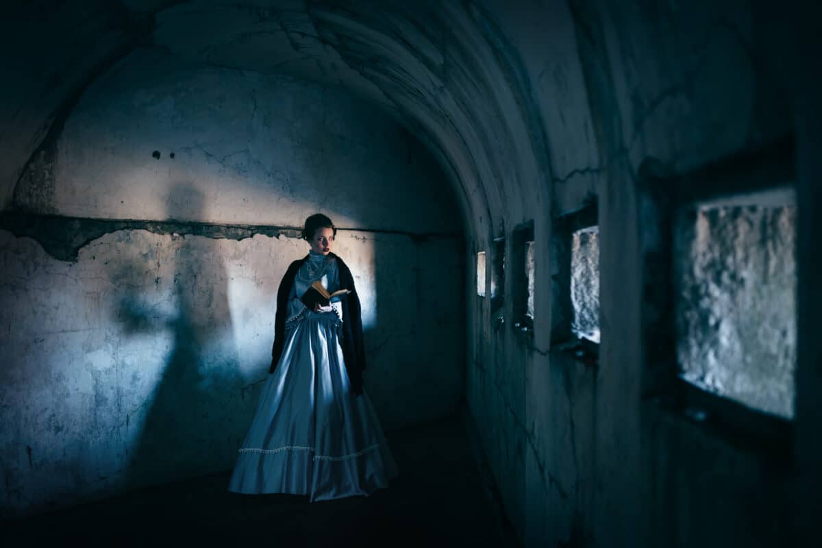 Woman in victorian dress standing alone in a dark room in a castle