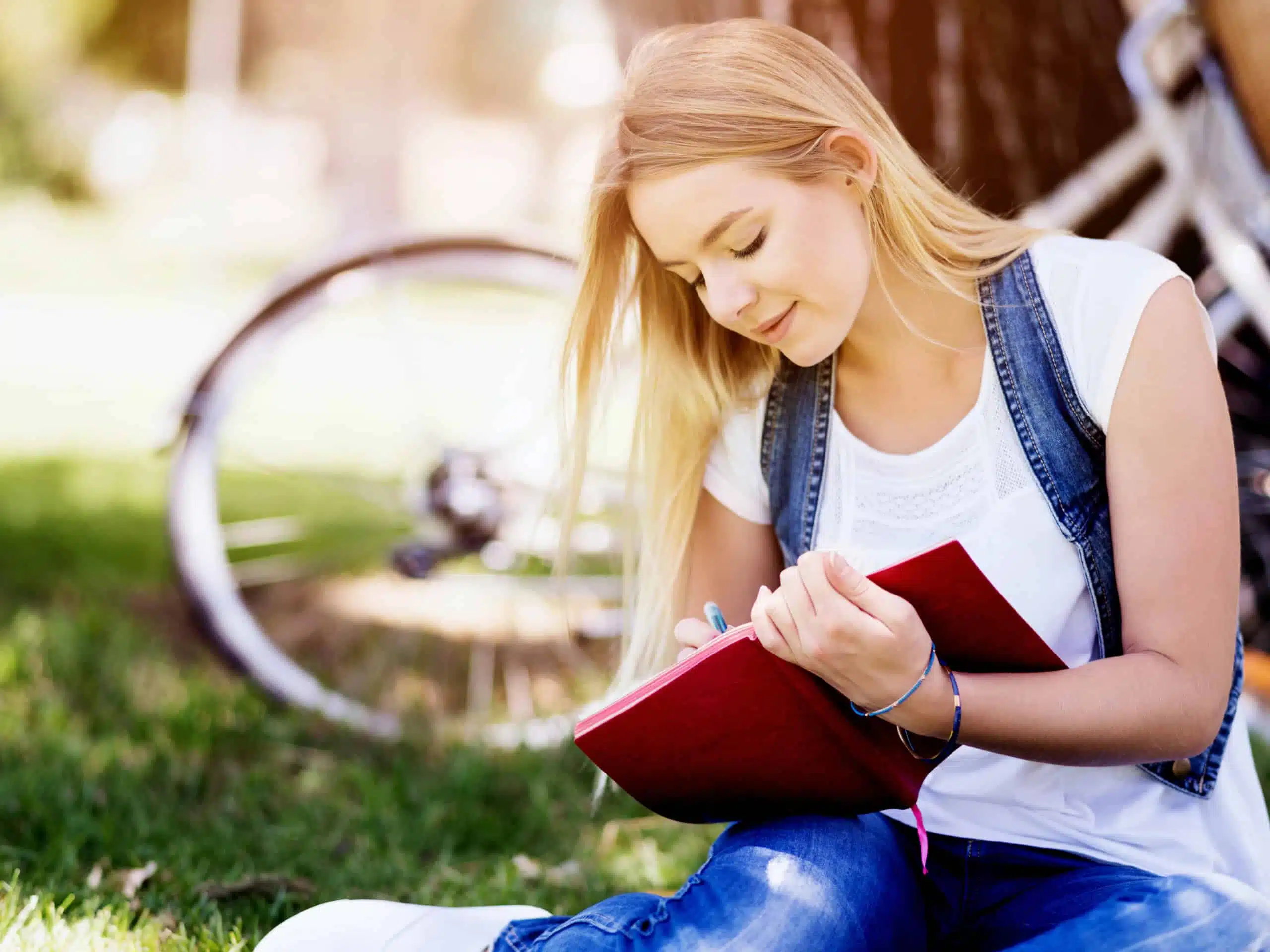 Beautiful young woman writing in her diary outdoors