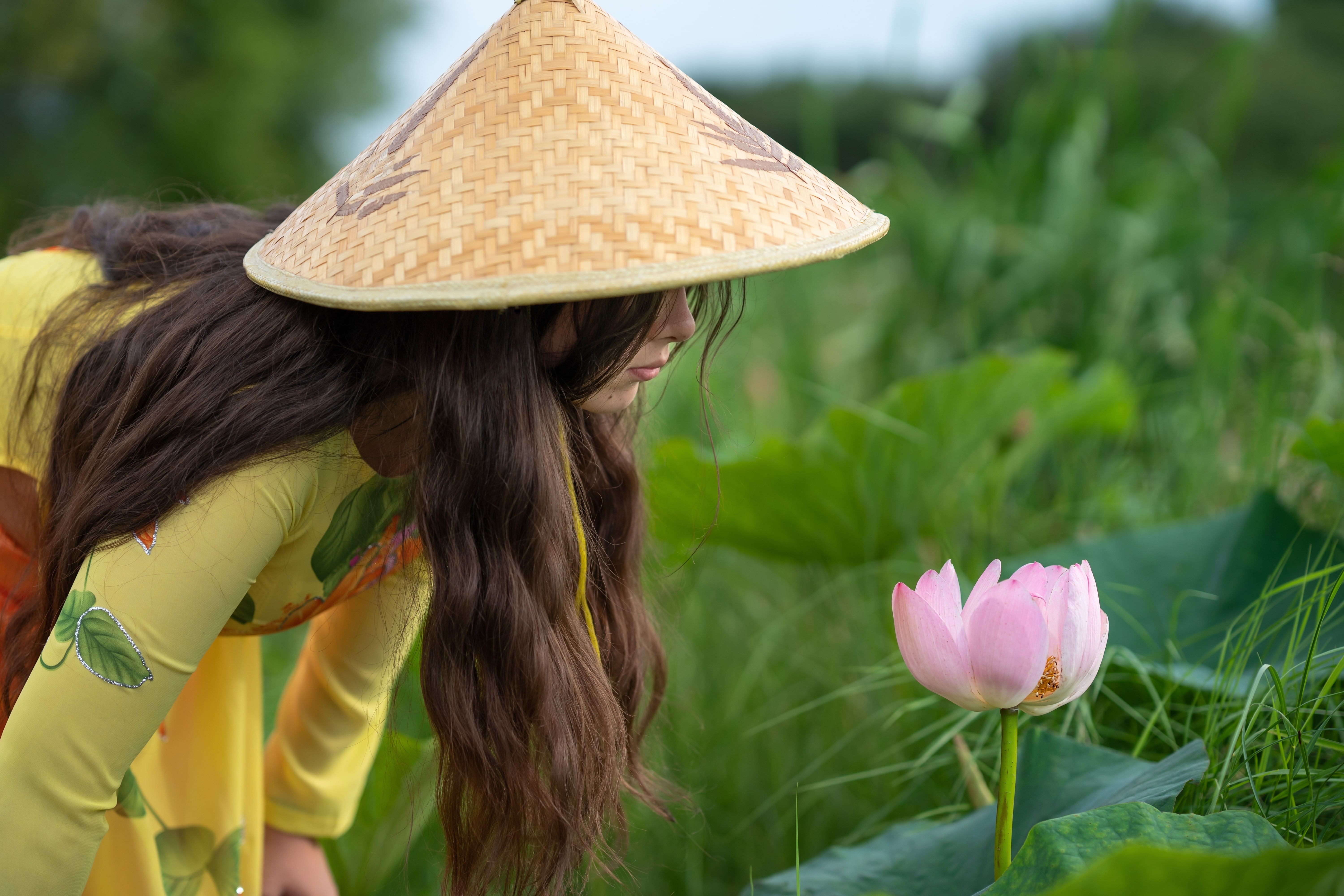 Beautiful girl wearing a traditional hat and dress in lotus flowers garden