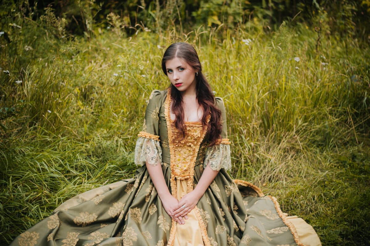 Young beautiful girl in a green rococo dress is sitting in the field