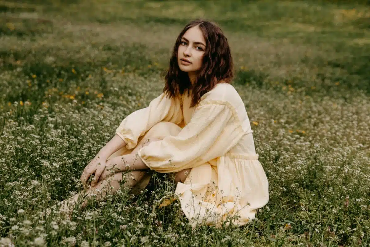 sad lady in summer dress sitting on the grass with yellow wildflowers