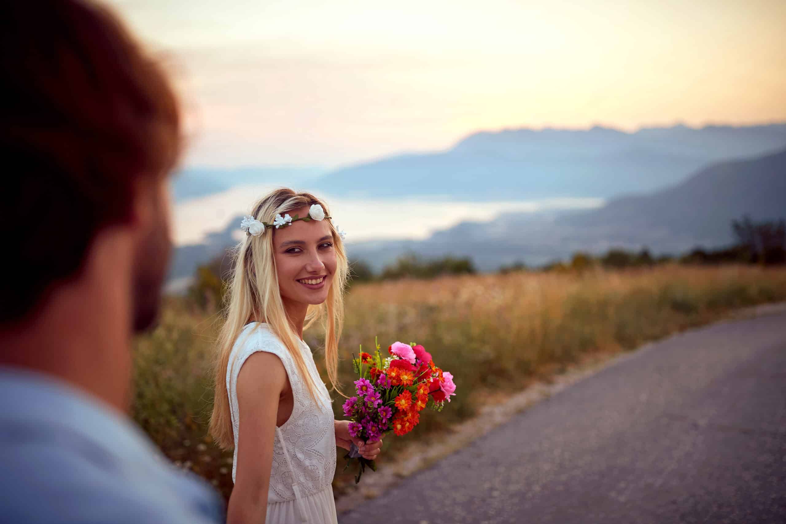 Boho style bride with bridal bouquet leading groom on road outdoor down the mountains.