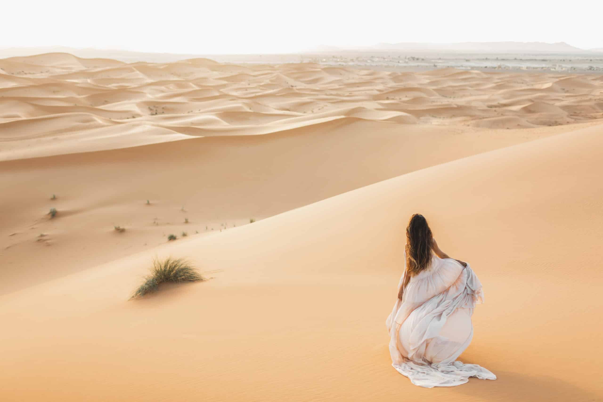 woman in flowy white dress walking in the desert in daylight