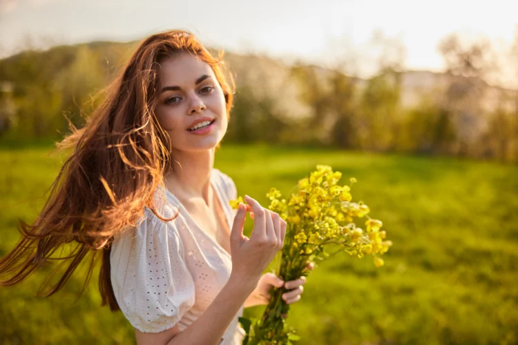 woman with a bouquet of wild yellow flowers in the rays of the setting sun in a field