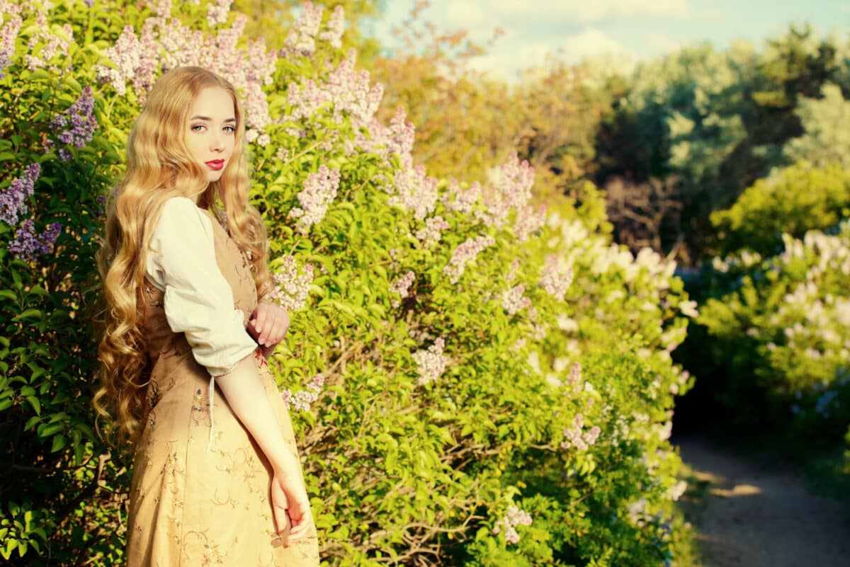 lovely young woman with magnificent blonde hair near blooming lilac in the countryside