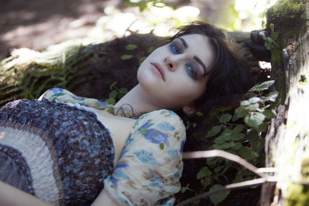 young beautiful woman with magical blue eyes lying in the woods