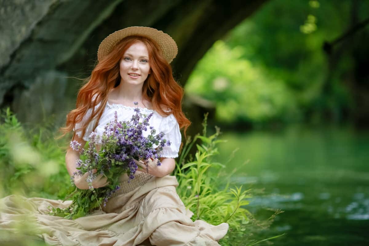 A woman sits on the Bank of the river in the forest and holds a bouquet of flowers in her hands